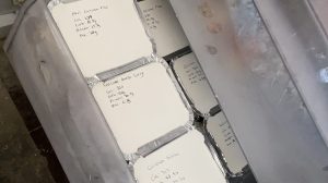 Photo of several small silver foil trays with white lids in a clear freezer drawer. The white lids have various meals and nutrition information written on them. 