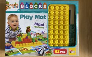A multicoloured box containing a toy is laid flat on the floor. The box has a white baby on the front playing with building blocks and the animal cut outs which the toy contains. 