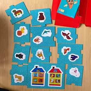Photo of playmat pieces with the backs various animals and 2 houses. The pieces have a blue background with white polka dots. 