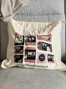 A beige drawstring bag with various black and red images on featuring various airport codes, cities and timezones on. 