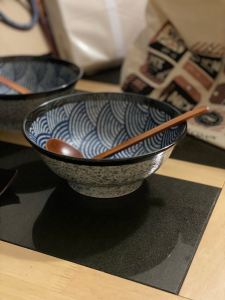 2 blue and white bowls with brown wooden ladles inside are sitting on a light brown wooden table with black quartz marble rectangles on the table top. 